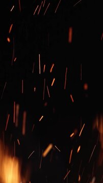 Glowing sparks rising from burning firewood at night, illuminating the darkness with warm, flickering light. Close-up and slow-motion shot on black background
