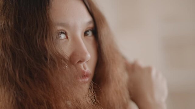 Adult woman shown in close three-quarter profile turning head right, long textured hair flowing across cheek and lips, eyes looking off frame under warm side light in soft indoor setting