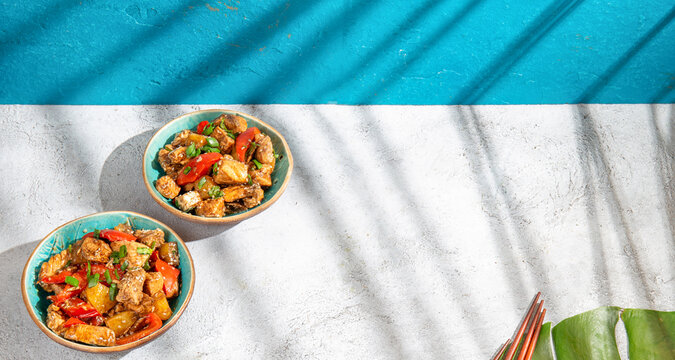 Hawaiian pinapple chicken in blue bowls on white background. Sunlight effect