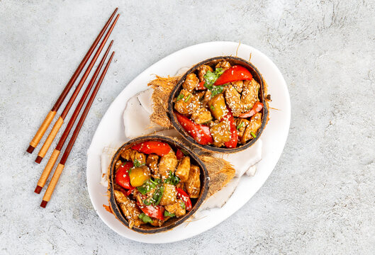 Hawaiian pinapple chicken in natural coconut shell plates on white background