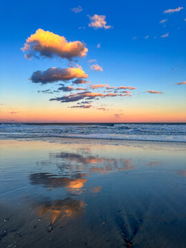 Colorful sunset clouds reflected in wet sand on the beach down the Jersey shore in Bradley Beach, New Jersey Monmouth County with breaking waves in the background
