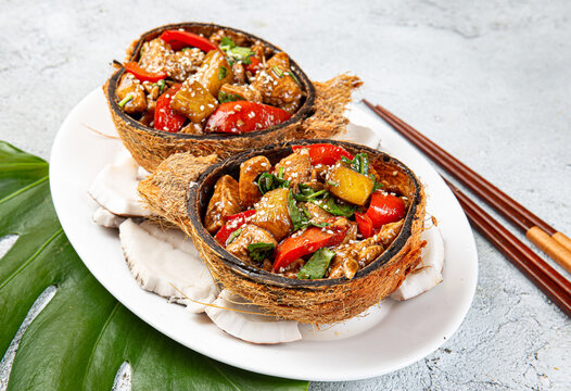 Hawaiian pinapple chicken in natural coconut shell plates on white background