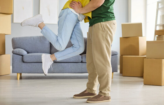Couple embrace while moving home among boxes. Man and woman celebrate relocation in a bright apartment, showing love and joy by a sofa and cartons. Concept shows love home and relocation.