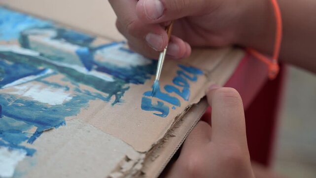mani di un giovane pittore dipingono con un pennello su di un cartoncino con dei colori ad acqua