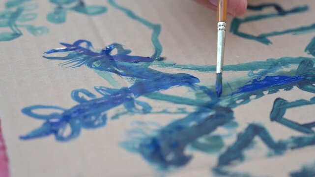 mani di un giovane pittore dipingono con un pennello su di un cartoncino con dei colori ad acqua
