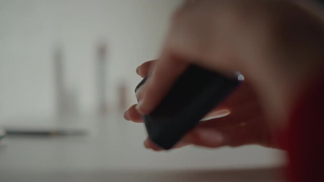 Profile view of woman pressing makeup sponge along jawline while hands hold slim rectangular object nearby, with subtle mouth movement, poised fingers, soft light, and focused beauty care