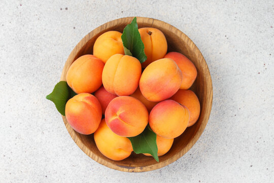 Top view of fresh ripe apricots in rustic wooden bowl with green leaves on stone gray background. Healthy seasonal summer fruit, healthy food, natural nutrition, ingredient for cooking and desserts.