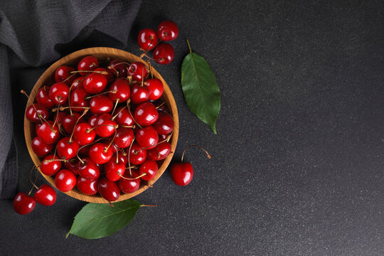 Fresh ripe sweet cherries in rustic wooden bowl with green leaves on black textured background. Top view flat lay with copy space. Juicy organic summer fruit, red berries, healthy seasonal food