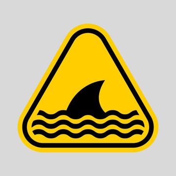 Yellow triangular warning sign featuring a shark in water, indicating marine danger and potential shark attack risk.