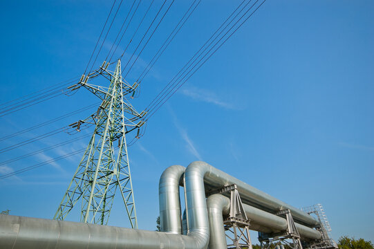 The photo shows a pipeline and a power transmission tower against a blue sky