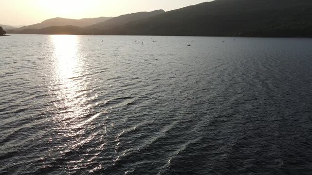 Aerial Tracking Back over the Shore of Loch Venachar past a Pirate Flag, Paddleboarders Beyond