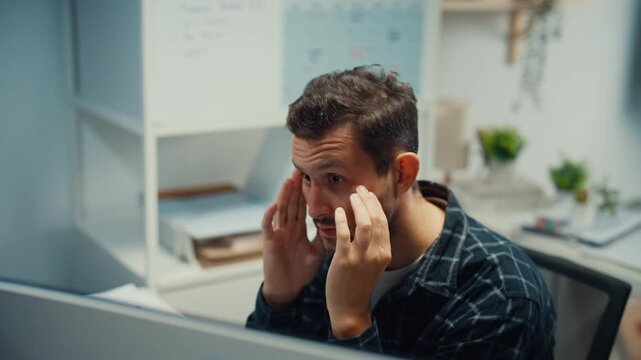 Young Caucasian male programmer writes code using multiple screens in home office workspace. AI development, cybersecurity, network database system, software engineering, remote tech startup concept.