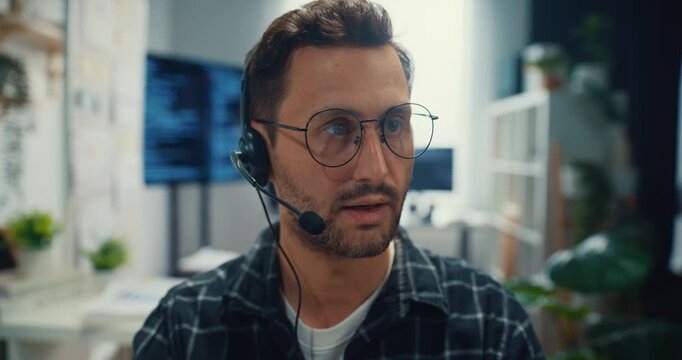 Young Caucasian male technical support specialist wearing headset speaks on computer at office. Professional call center help desk, Cyber security operator service, Online client consultation concept.