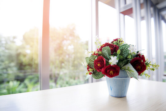 Artificial Flower Arrangement in Blue Pot on Table by Bright Window