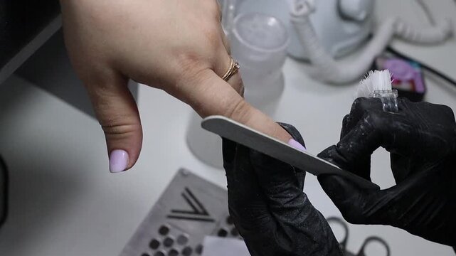 Nail technician shaping a client's fingertip with a file to create a rounded contour. Professional manicure footage for beauty services, nail care, tutorials, training and salon advertising.