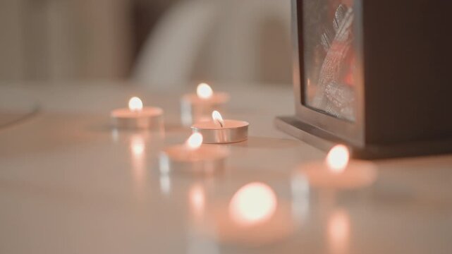 Low angle view shows tealight candles arranged across smooth tabletop, central flames crisp while near and far candles fade into soft bokeh, creating warm, peaceful interior atmosphere