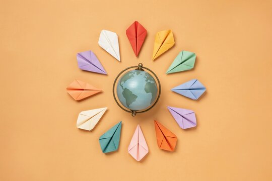 Origami paper airplanes circling globe, colorful folded planes, travel concept with world map, paper craft copy space