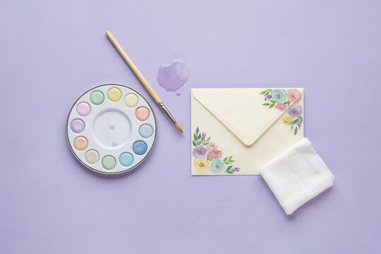 Soft lilac background, pastel watercolor gardening tools and letter, paint palette, brush and floral envelope arrangement with copy space