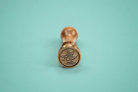 Vintage wooden rubber stamp on turquoise background. Retro office supplies with carved bird motif. Antique wood handle seal with green backdrop. Handcrafted insignia for creative projects.