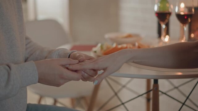Close view of two people exchanging small object over wooden round table, with hands meeting palm to palm, fingers adjusting grip, and soft blur suggesting ongoing handover in warm intimate setting