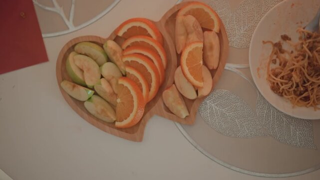 Overhead composition showing heart shaped wooden bowl filled with alternating orange and avocado slices beside round plate holding shredded garnish on patterned placemat, creating fresh colorful