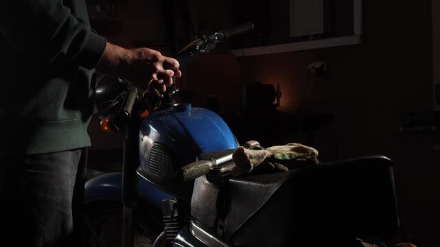 Man checking instructions on a smartphone while repairing a vintage motorcycle in a home garage, focusing on maintenance and repair work with a classic vehicle