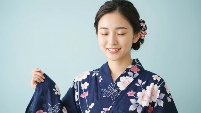 青い背景の前で紺色の浴衣を着て笑顔を見せる女性