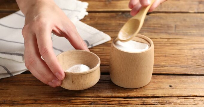 Woman pouring baking soda into bowl at wooden table, closeup
