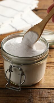 Woman taking baking soda with spoon at wooden table, closeup