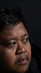 A dramatic side profile portrait of an adult Southeast Asian male looking away to the left side with a highly focused expression on a dark black background. The gentleman is wearing © M. Faisal Riza