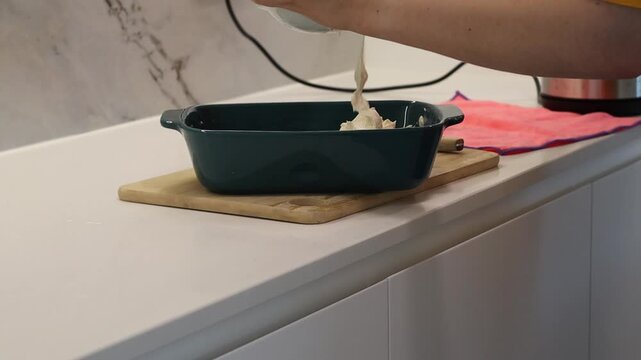 Woman placing dough into a dark baking dish in a home kitchen. Cooking footage for recipe videos, baking tutorials, food blogs, culinary articles, homemade desserts and kitchen content.