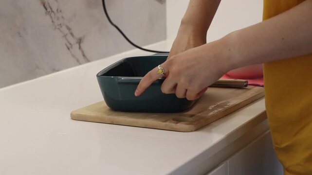 Close view of a woman greasing a dark baking dish with oil before cooking. Home kitchen footage for recipe videos, food blogs, baking tutorials, cooking content and culinary articles.