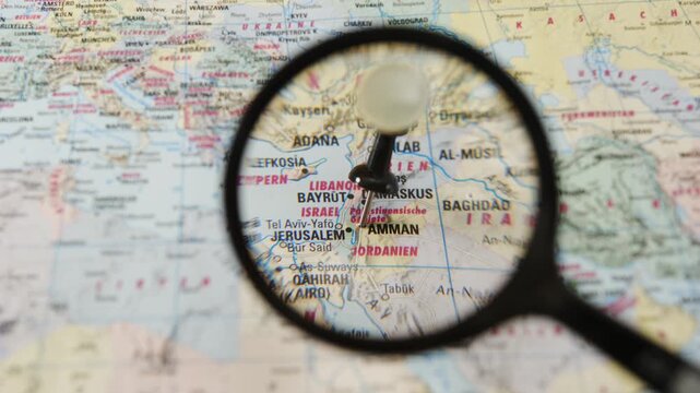 Magnifying glass locating Amman on a printed paper map