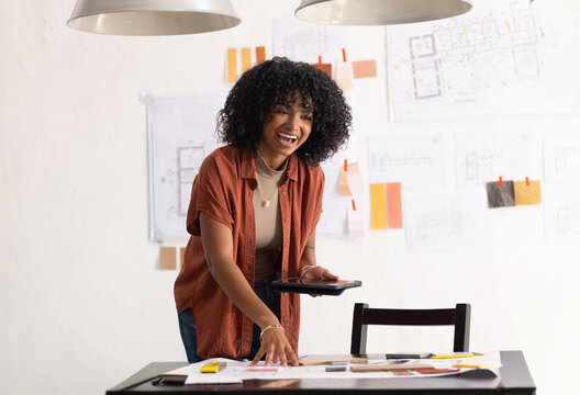 African American woman in rust top examining plans holding tablet with swatches at design studio
