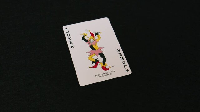 Hand flipping a face down playing card to reveal a joker on black