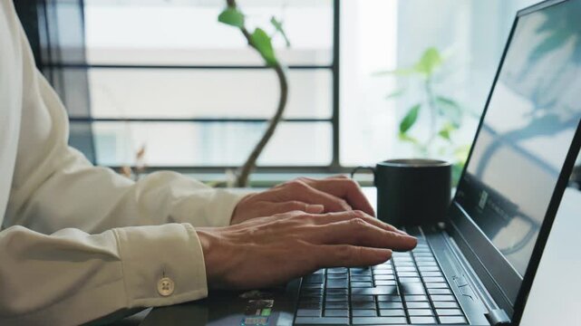 Side close-up of hands typing on laptop then clasping by bright window