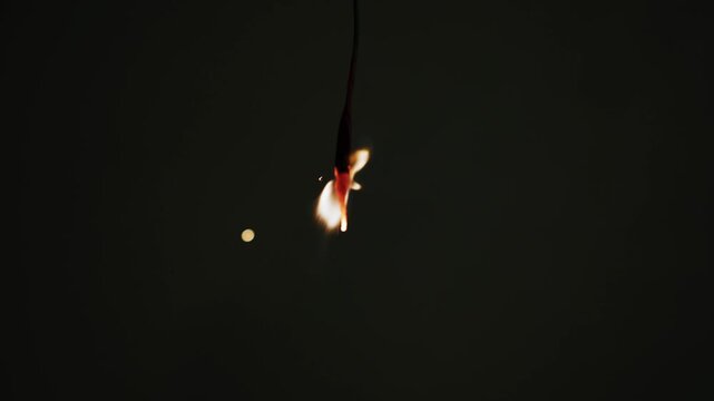 Small flame on a hanging string burning down to a glowing red ember in darkness