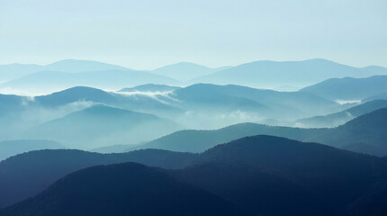 Fototapeta premium Serene Blue Mountain Range with Fog Rolling Through the Valleys in a Misty Morning Landscape