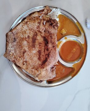 Traditional Malaysian breakfast thosai served with curry on a metal plate.