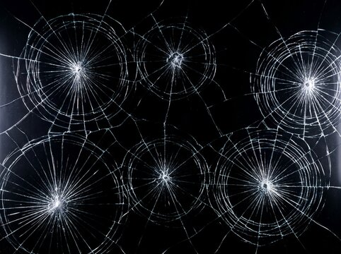 Cracked glass with radial impact points isolated on black background, shattered broken window texture for design overlay and background