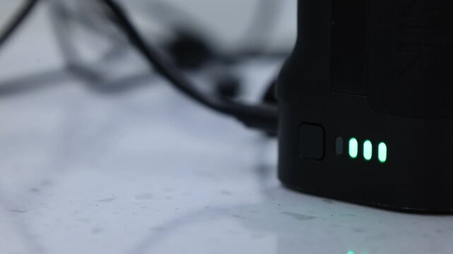 A close-up of a black portable battery or power bank with green LED indicator lights glowing on a desk surface.