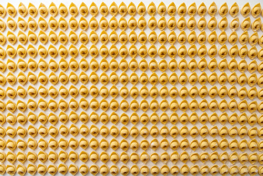 Countless rows of raw homemade italian cappelletti pasta perfectly arranged on a floured surface
