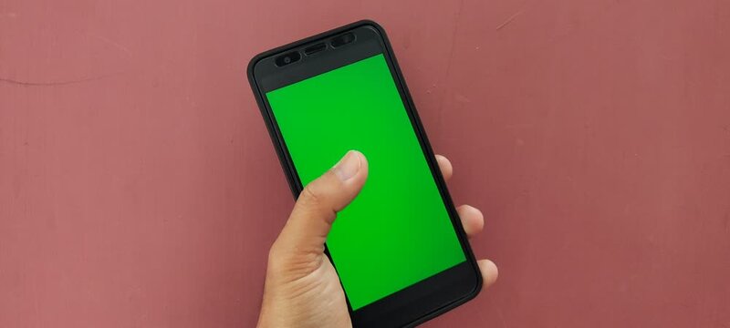 Hand holding a smartphone with a green screen background.