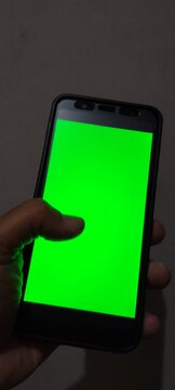 Close up of a hand holding a smartphone with a green screen.