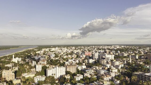 Vertical drone ascent in front of urban buildings in Kushtia, Bangladesh, capturing the city's buildings and green surroundings as the camera rises toward the open sky.