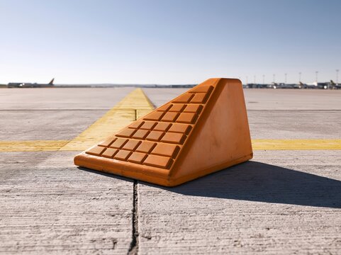 Single aircraft wheel chock on the apron in bright daylight demonstrating its grip and shape