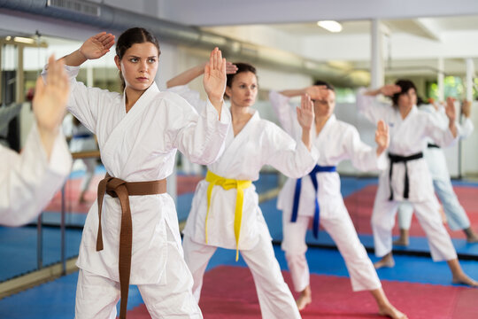 Women athletes learn practice of kata karate punches, hone fighting skills by repeated repetition. In gym, master coach during karate kata lesson with team students group, kata formation position.