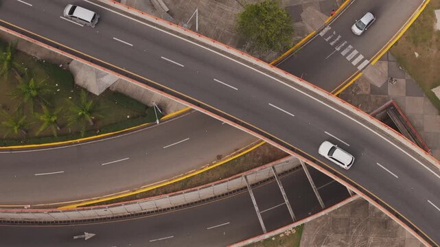 Top-down drone shot of cars driving over a curved highway overpass and multi-level interchange