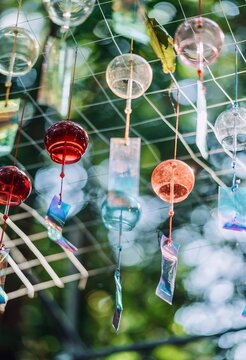Close up view of colorful glass wind chimes hanging outdoors with soft bokeh background.