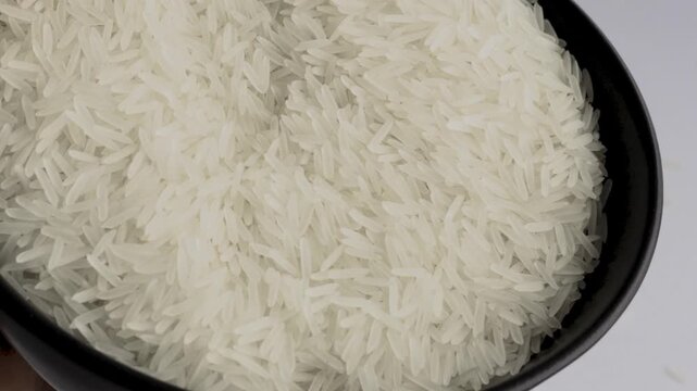 White basmati rice grains pouring from black bowl top view macro, FHD